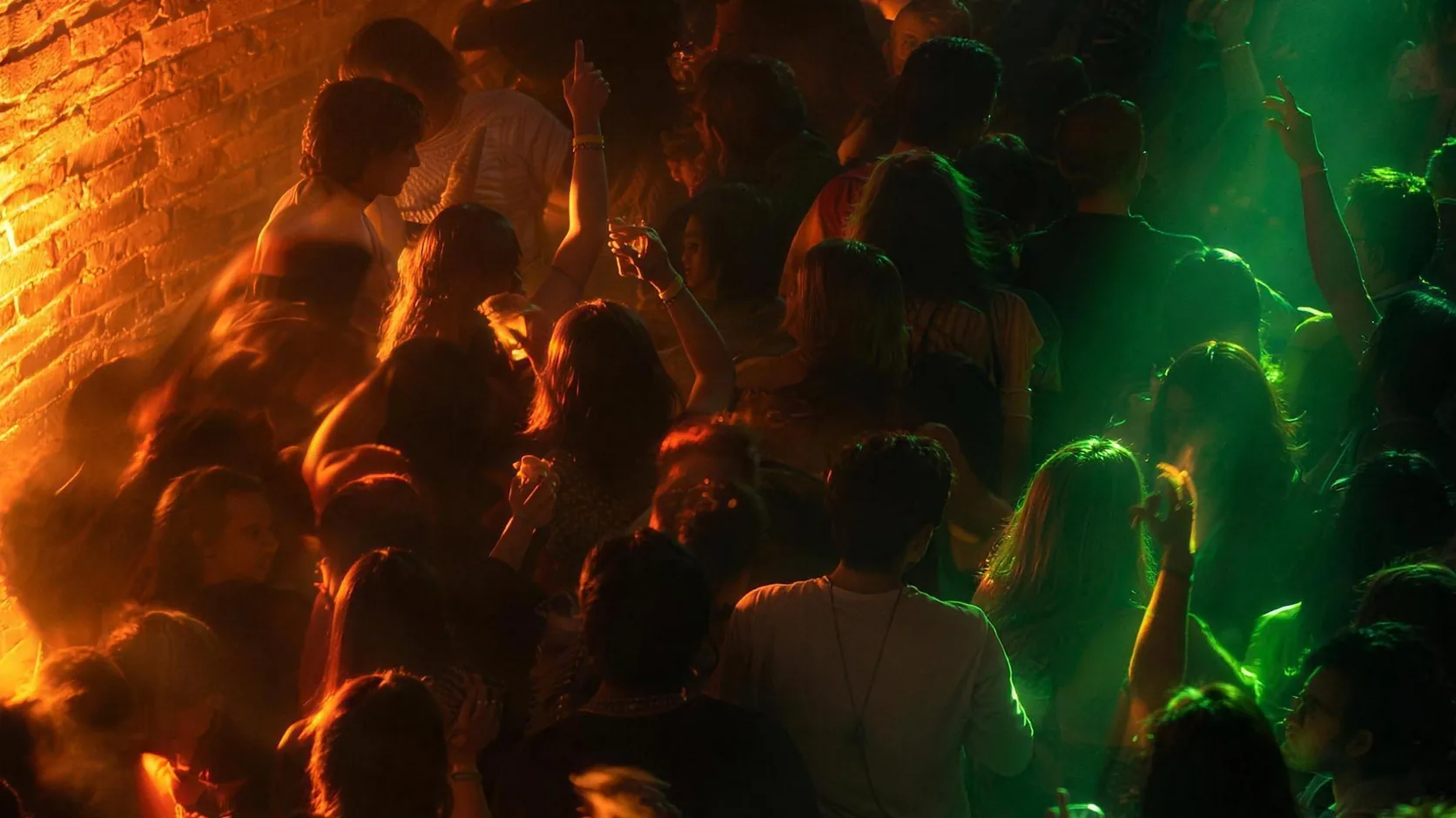 El salón de LOOP CLUB lleno una noche: el público bailando contra la pared de ladrillo, entre luz naranja y verde